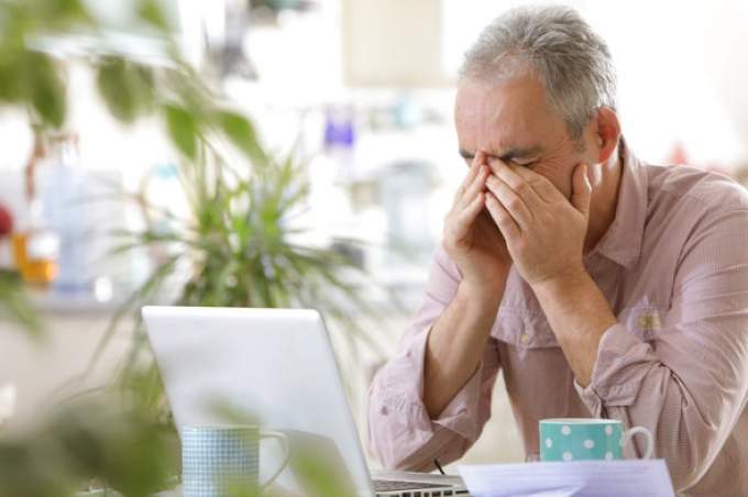 Man grieving and crying watching a funeral service live stream at a desk 