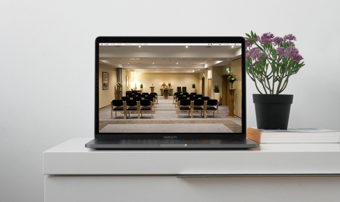 Funeral service stream on a laptop placed on a desk with flowers and books 